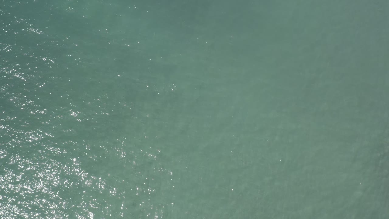 Murky green sea surface in Los Cabos, Mexico with subtle ripple bands, pale underwater streaking, and no visible people.