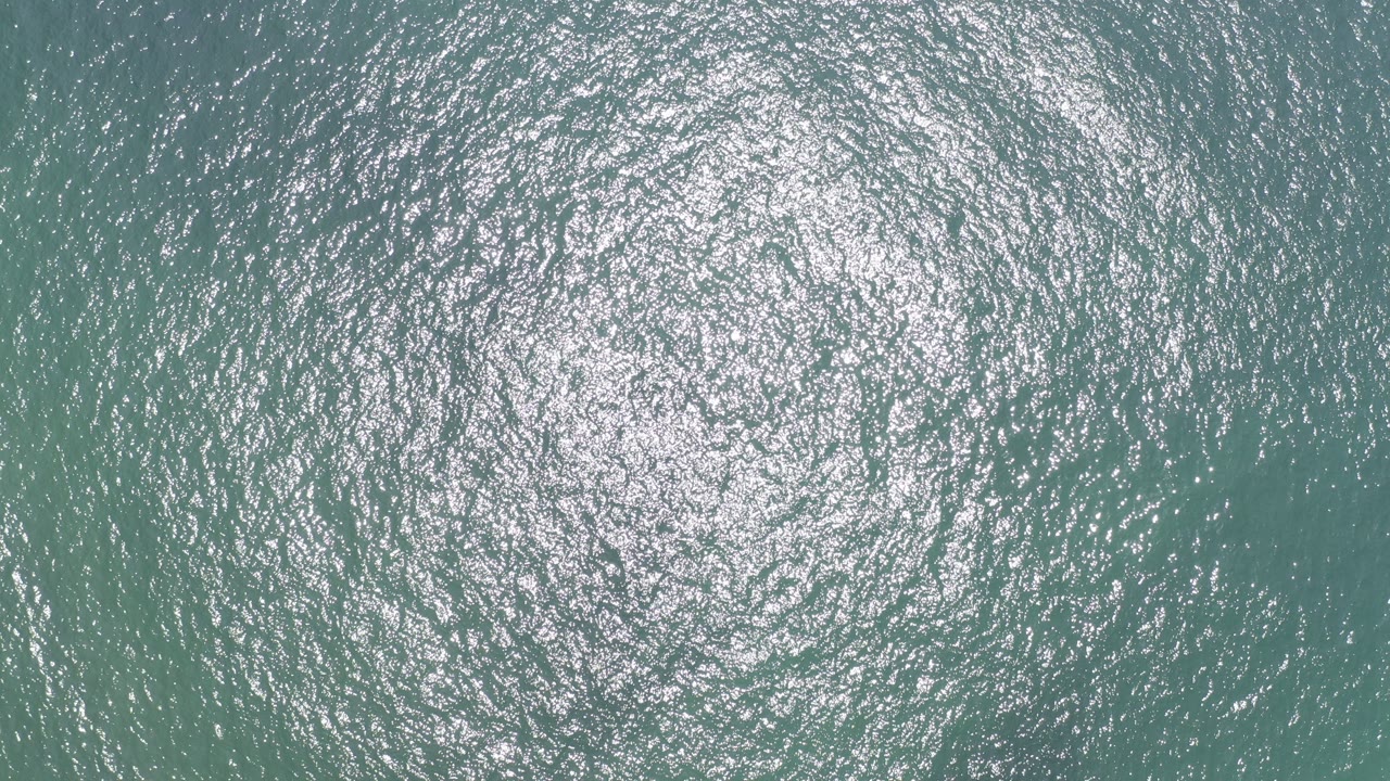 Overhead view of teal ocean water in Los Cabos, Mexico, with dense silver sunlight reflection near the upper left and no visible people.