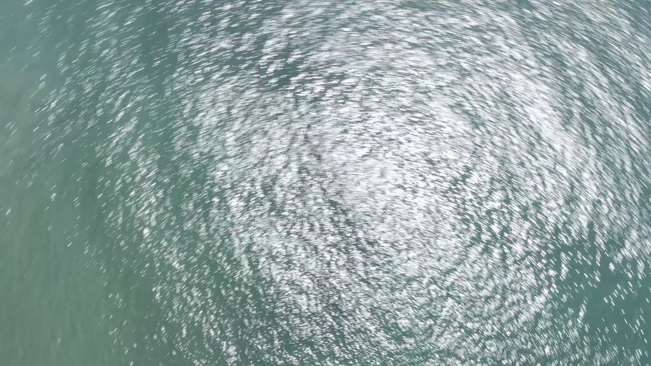 Aerial frame over green Los Cabos ocean water, filled with shimmering highlights and faint ripples, with no visible people.