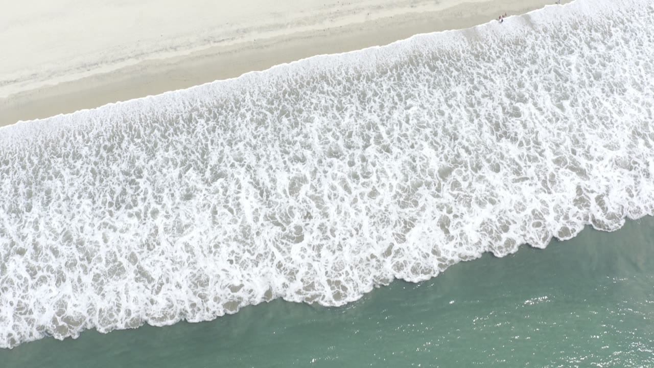 Wide overhead wave wash with white foam and green sea.