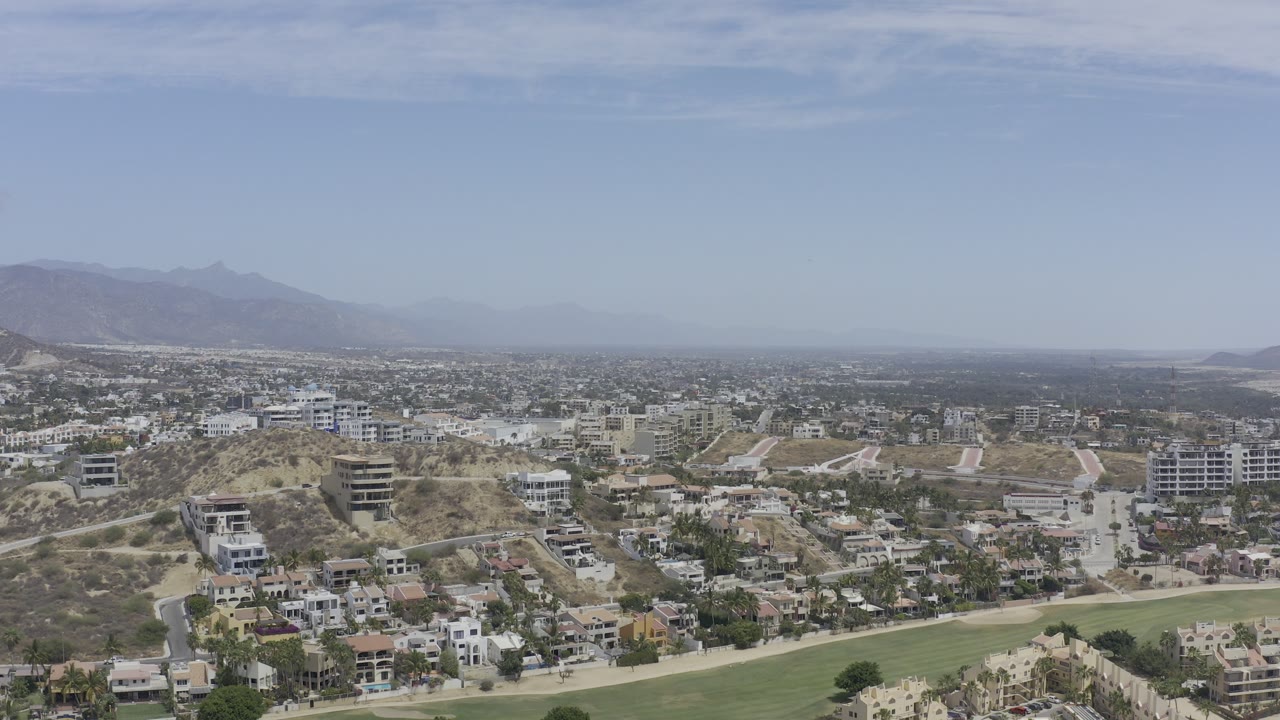 High city view with dry hills, modern buildings, road network, distant mountains, and broad sky.