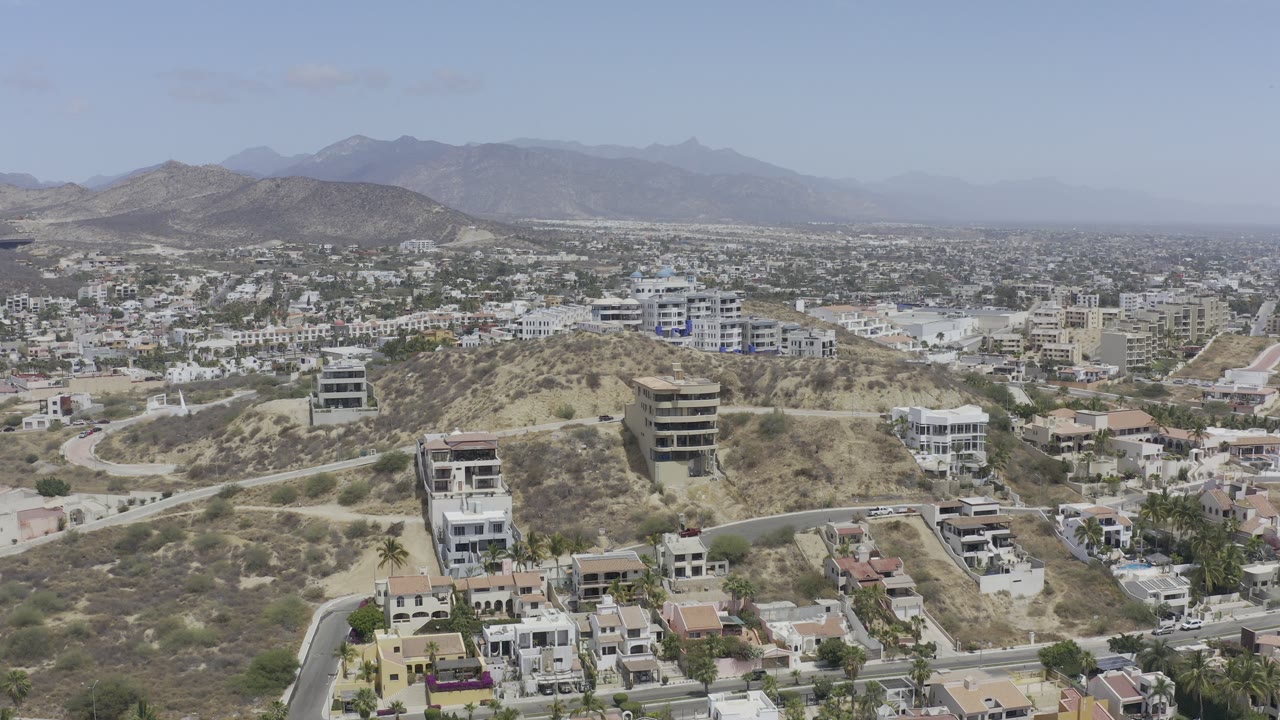 Drone view over hillside residences with a city plain and mountains in the distance.
