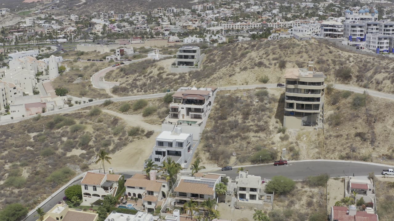 Aerial view of hillside houses, dry terrain, roads, and palm trees.