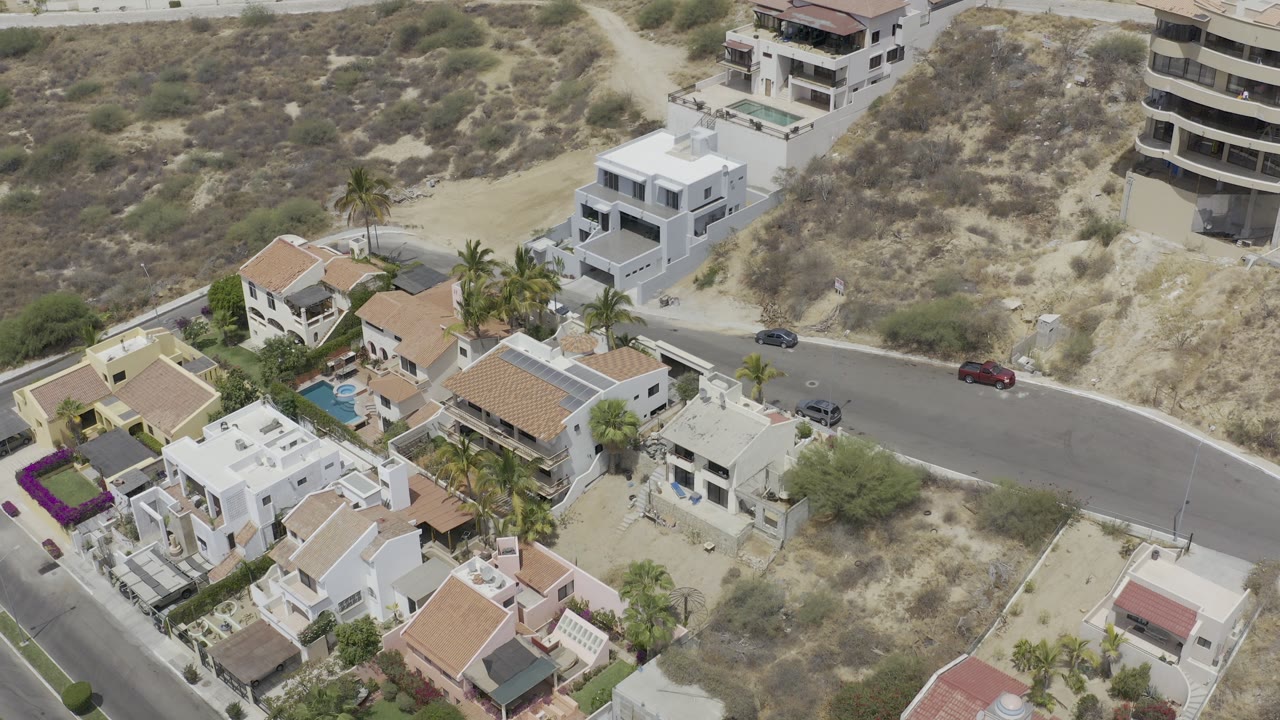 Aerial view of hillside homes, road, cars, pool, and dry terrain.