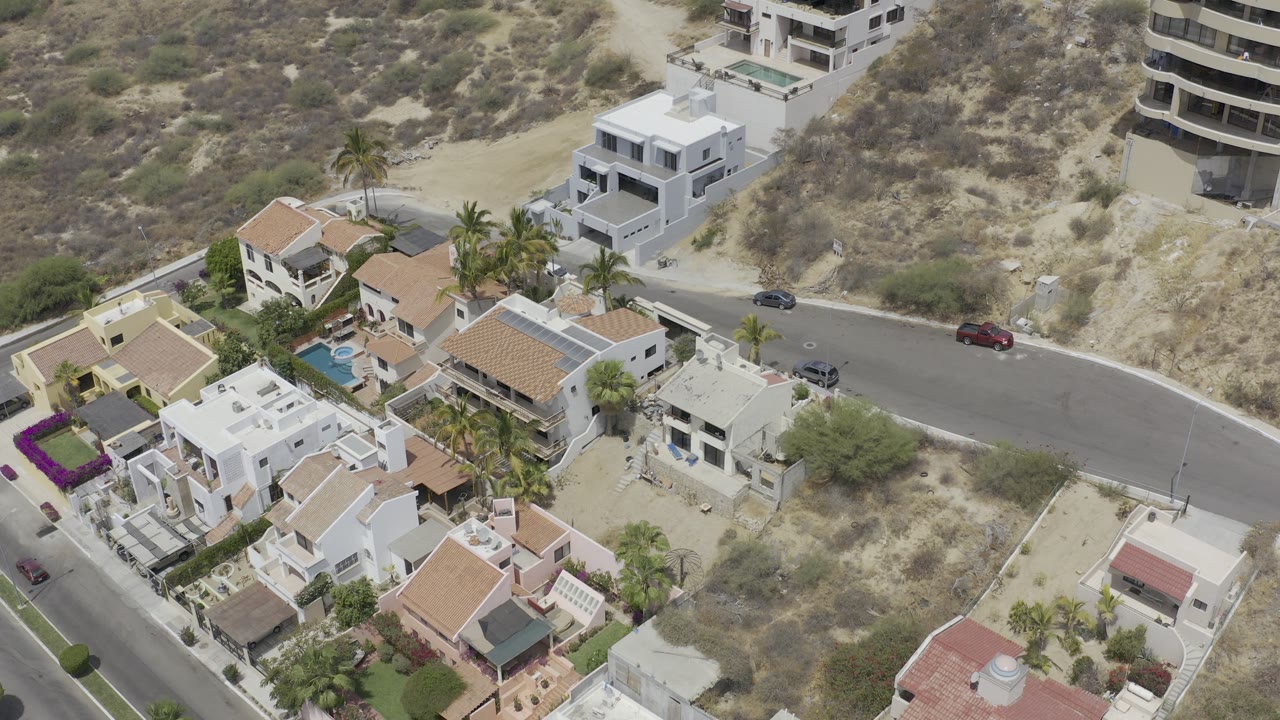 Drone view of rental houses and a curved street below a scrub-covered slope.