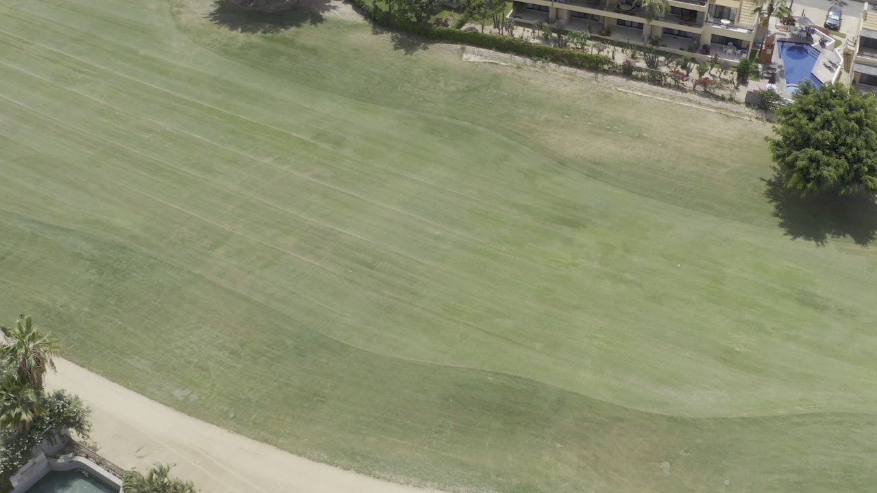 Aerial view of green mowed field beside a pale dirt road