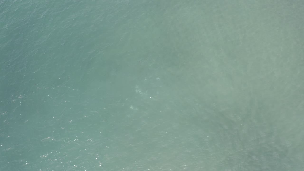 Overhead view of pale turquoise ocean water in Los Cabos, Mexico, with faint sand tones beneath the surface and no visible people.