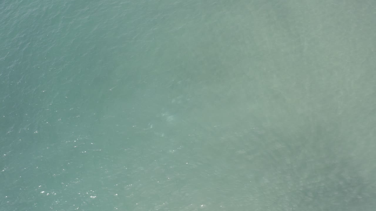 Pale ocean water with a muted sandy patch below the surface.