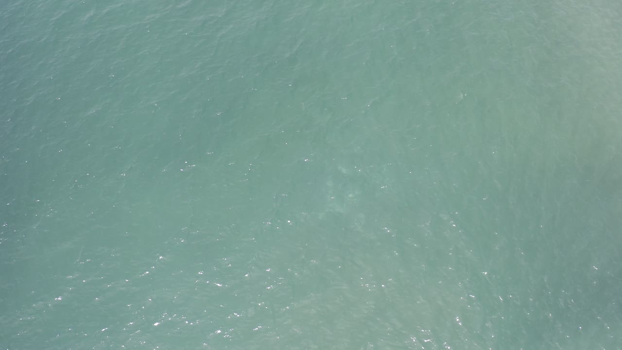 Green-blue water surface in Los Cabos, Mexico, with faint diagonal ripple texture and no visible people.