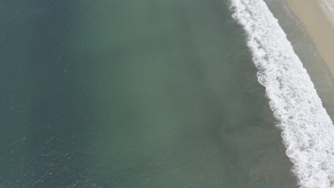 Blue ocean surface with white surf and sand along the upper right edge.