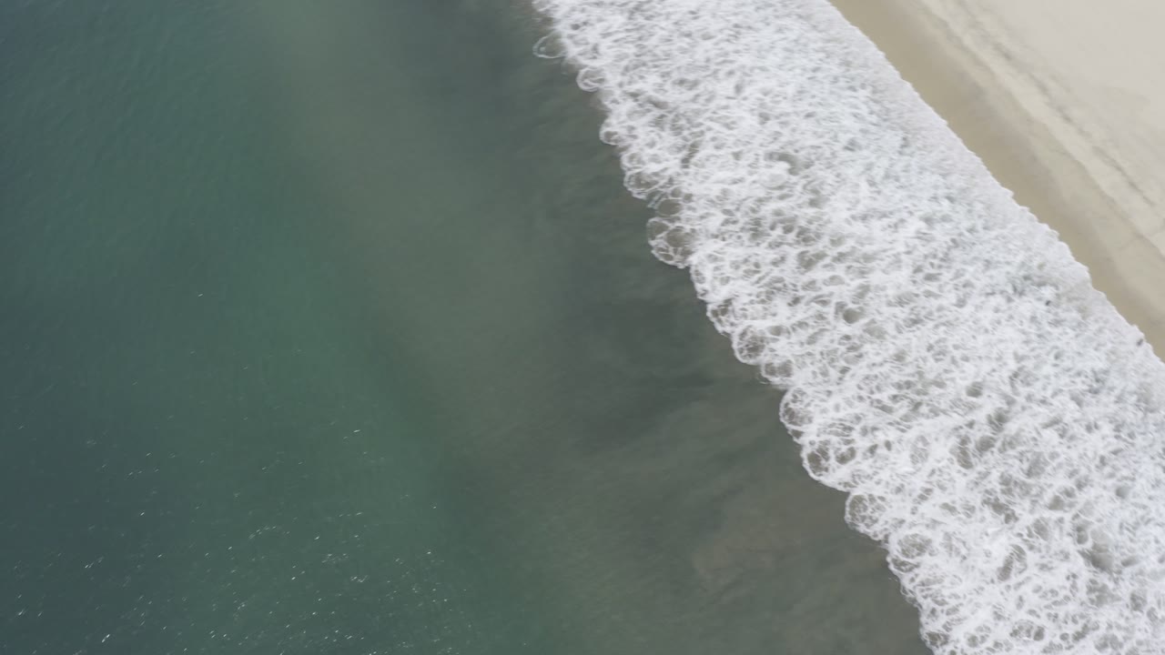 Overhead surf bands breaking beside a pale sand beach.