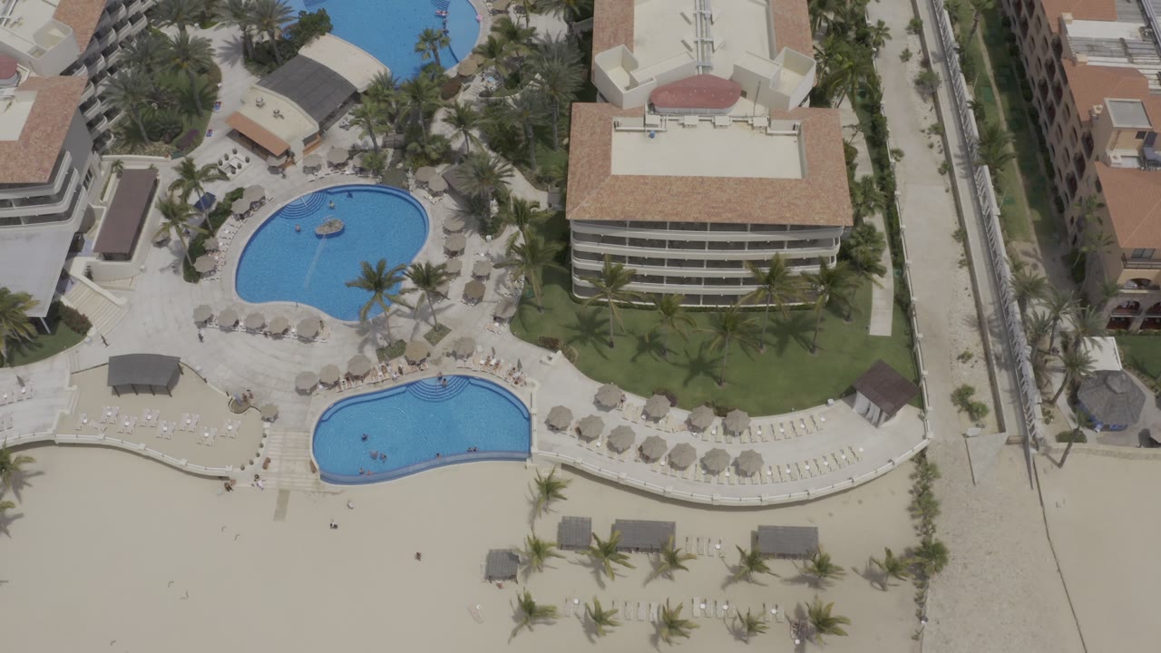 Top-down resort complex with pools, beach chairs, palms, and hotel buildings.