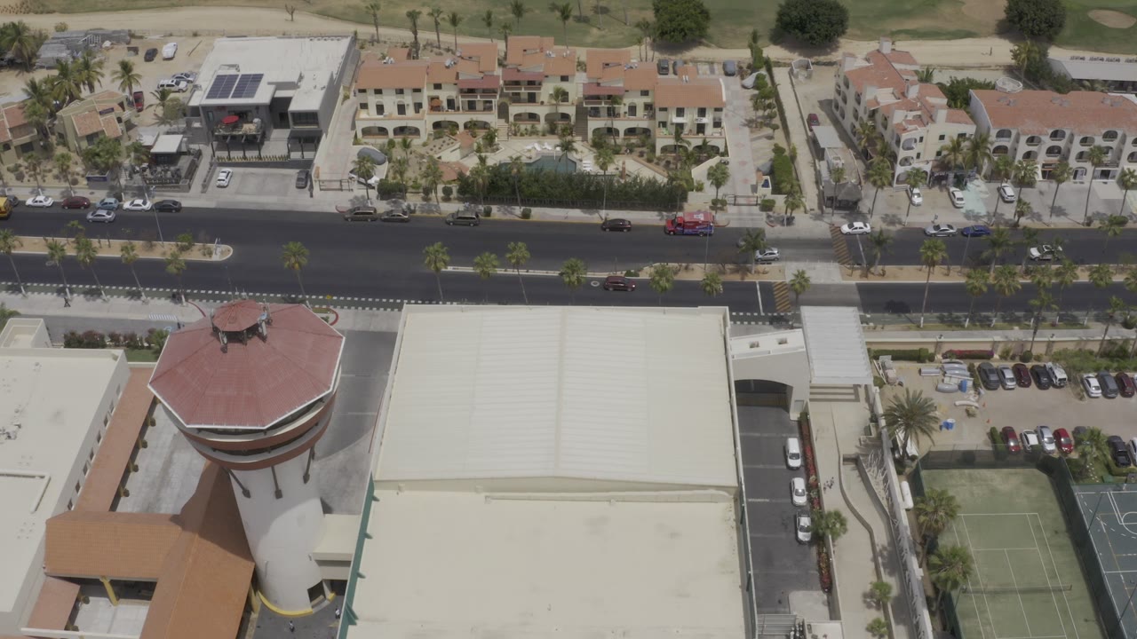 Aerial view of road, low buildings, tennis courts, and homes beside a golf course.