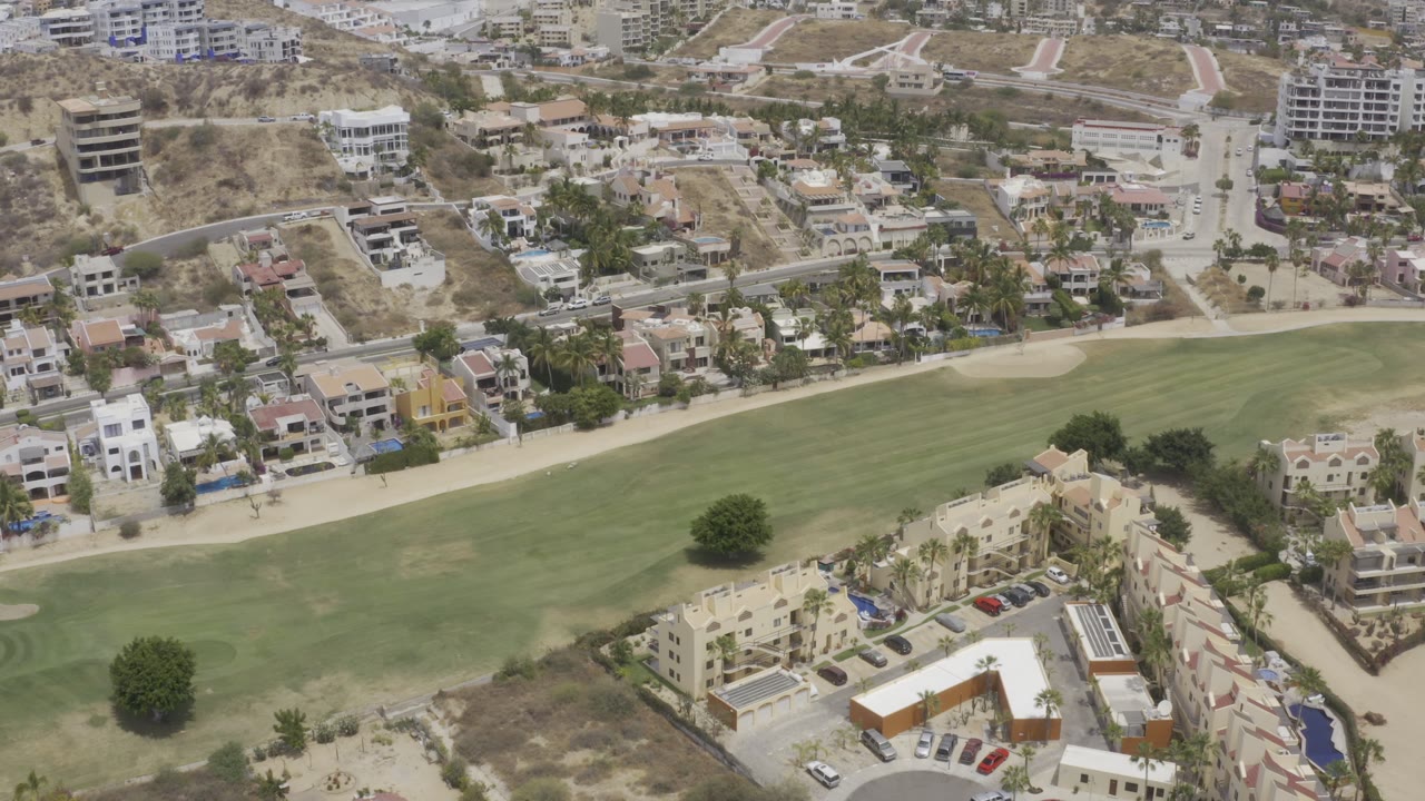 Drone-like aerial view of a golf course bordered by homes and desert hills.