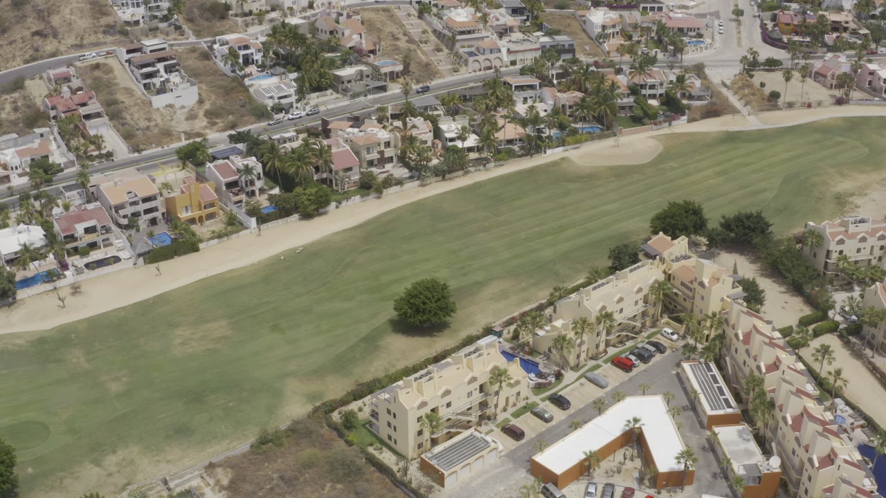 Aerial view of a golf fairway beside homes and apartment buildings.