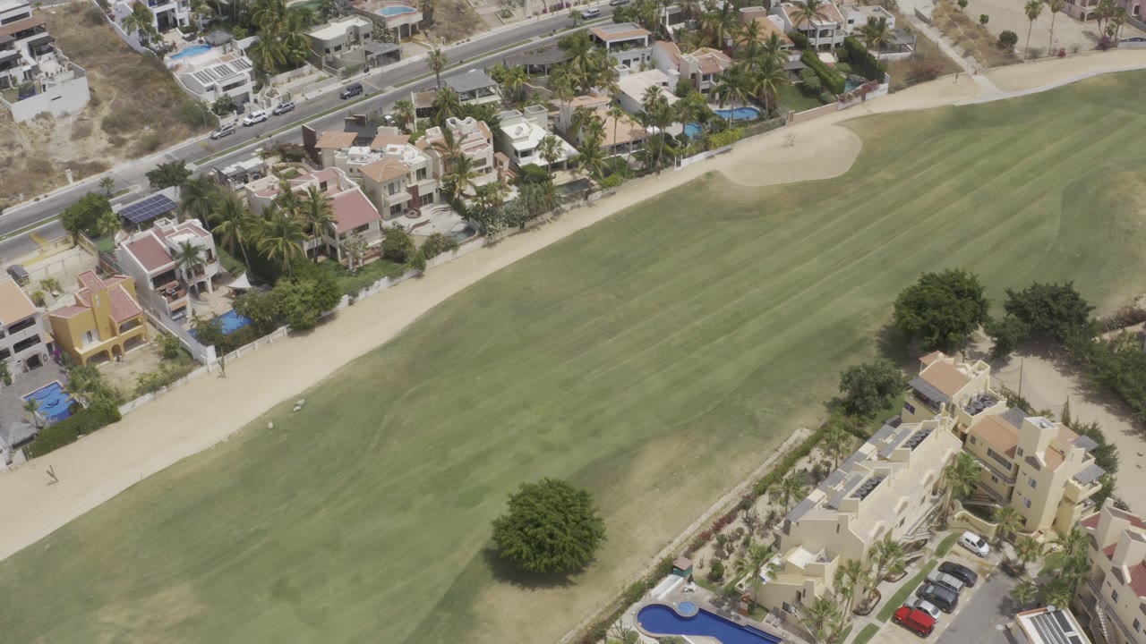 Overhead golf fairway with sand bunker, houses, trees, and parked cars.