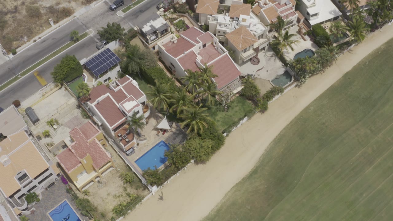 Overhead view of homes, pools, palms, road, and green ground.