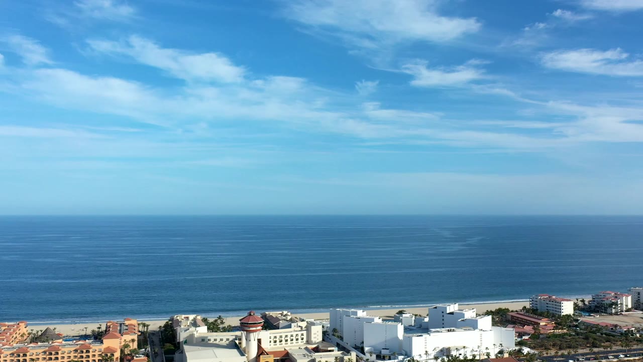 Blue ocean and beach with modern coastal buildings visible at the bottom.