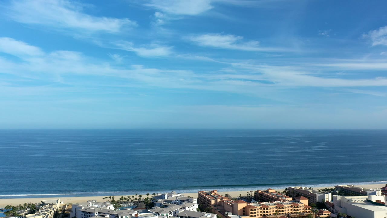 Wide blue ocean and beachfront buildings under a bright sky.
