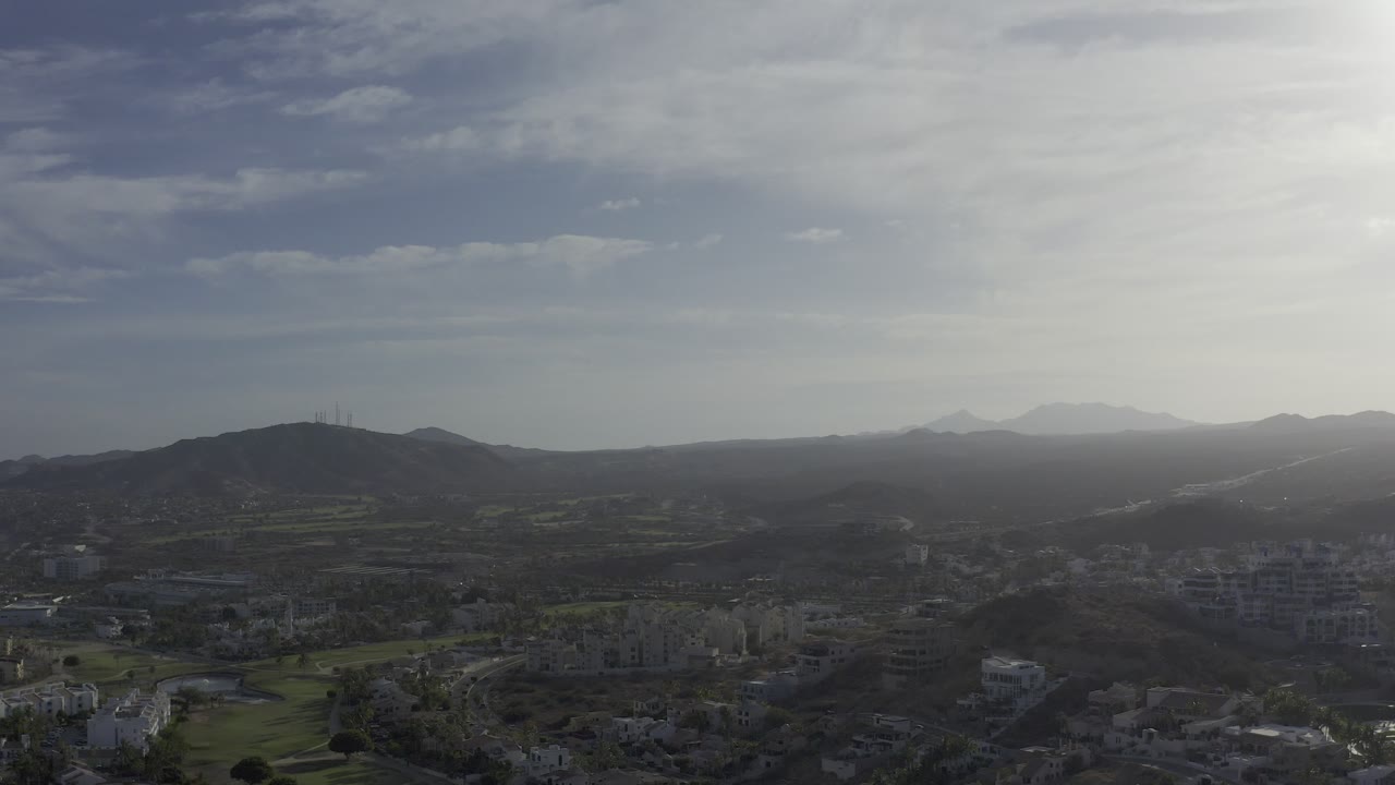 Wide aerial skyline with urban blocks and mountains in haze.