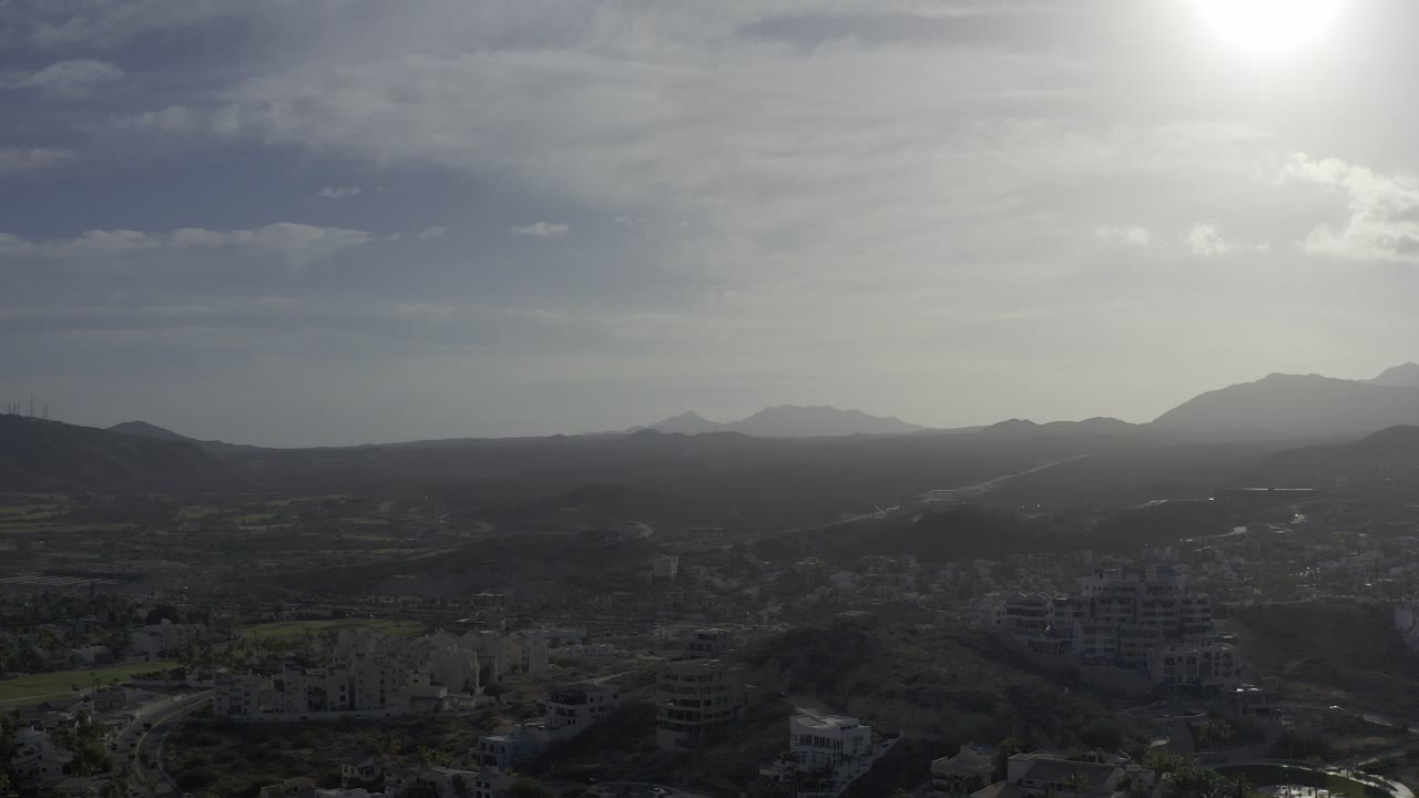 Aerial view of buildings, roads, hills, and distant mountains under bright sun glare.