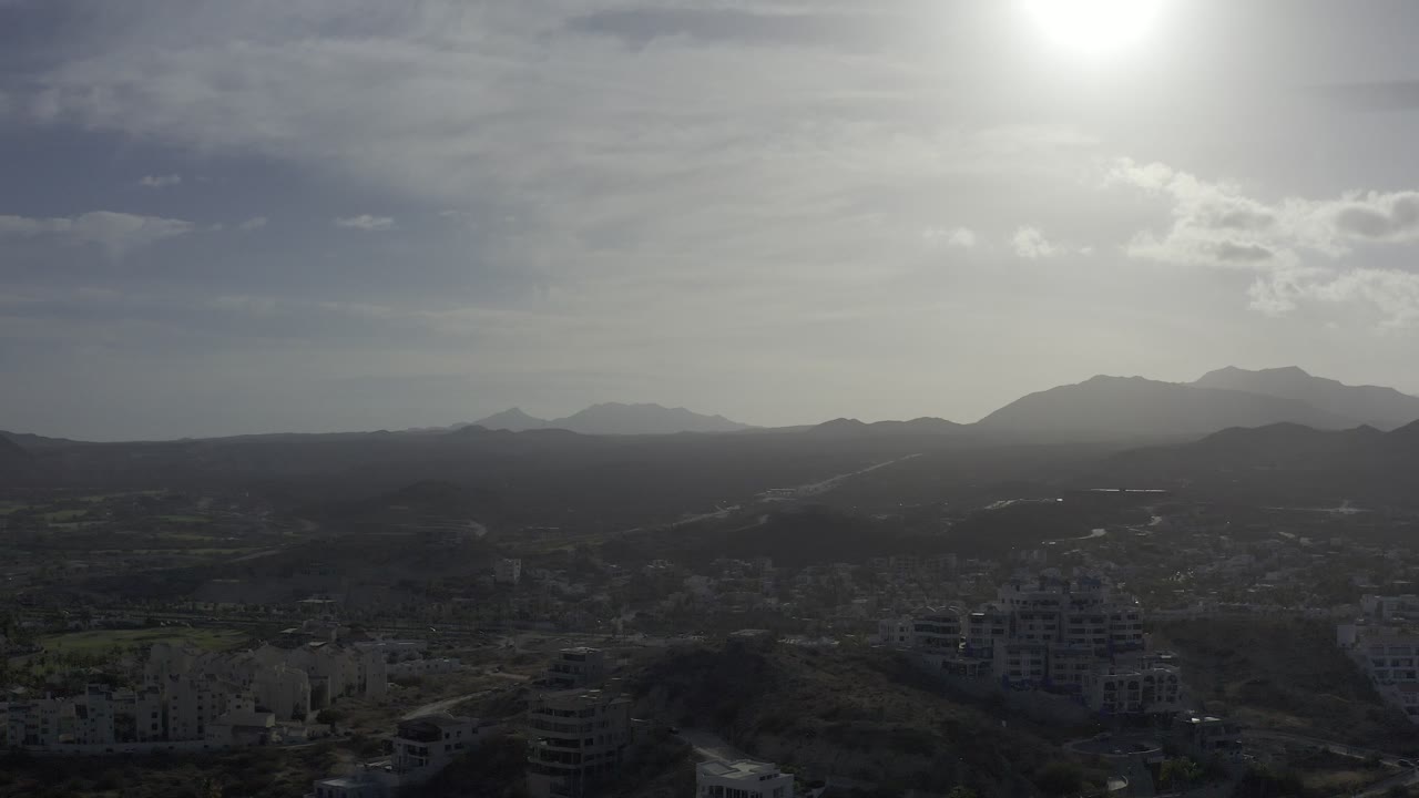 Wide aerial landscape with city below, dark hills, and bright sky.