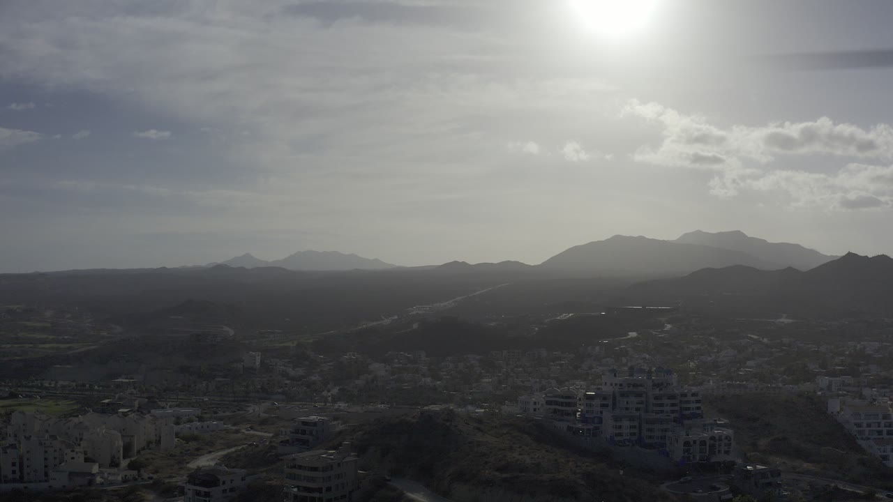 Bright sun over dark hills, distant mountains, roads, and buildings.