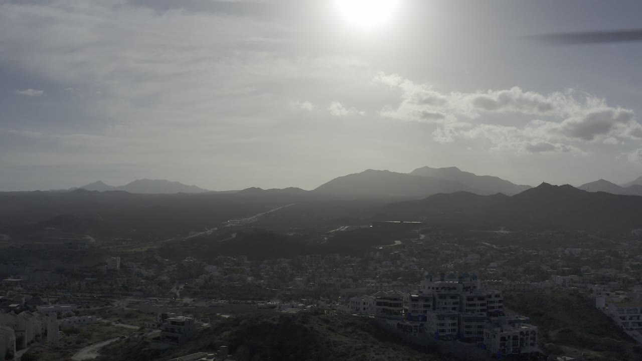Backlit mountain panorama above a city with rooftops and roads in the foreground.