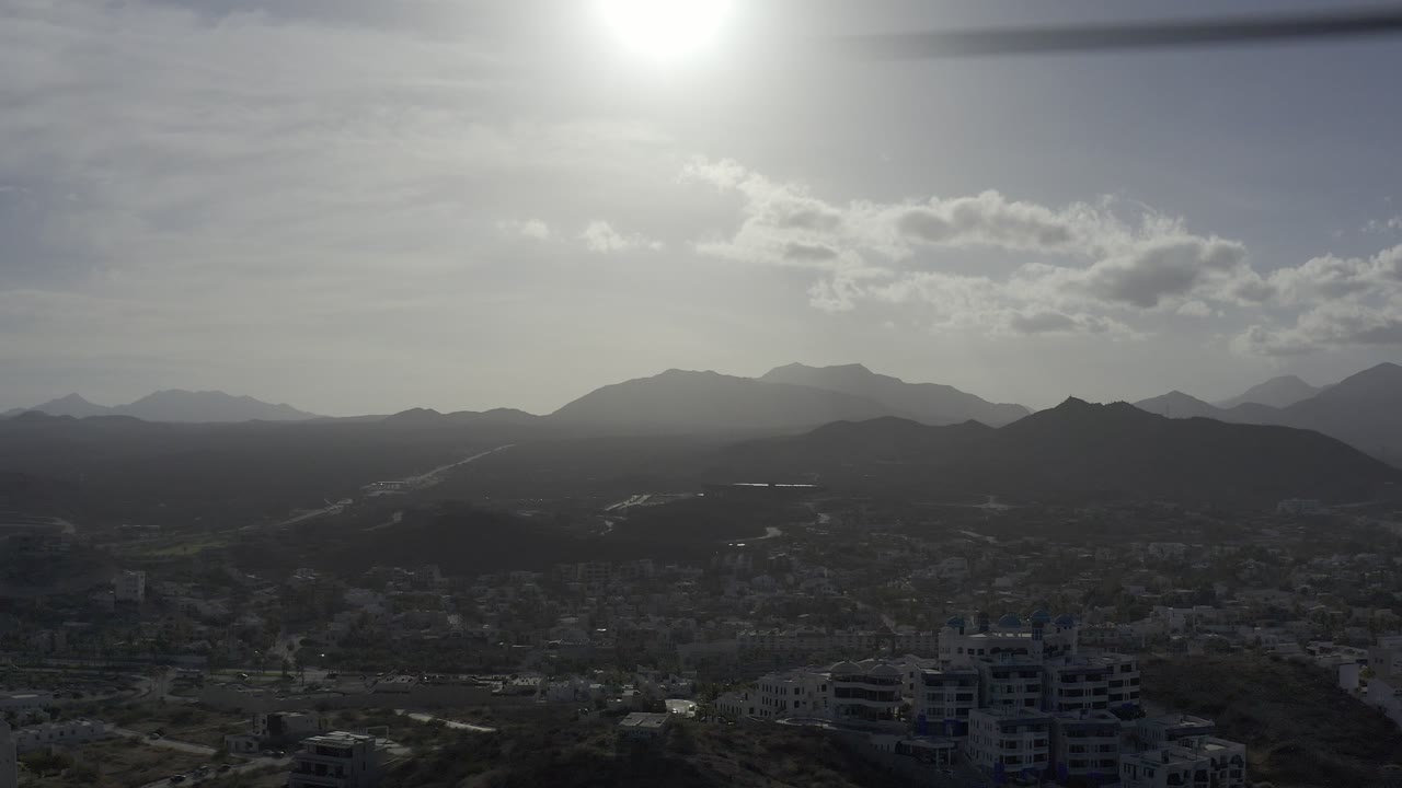 Aerial city view with foreground buildings and hazy mountain background.