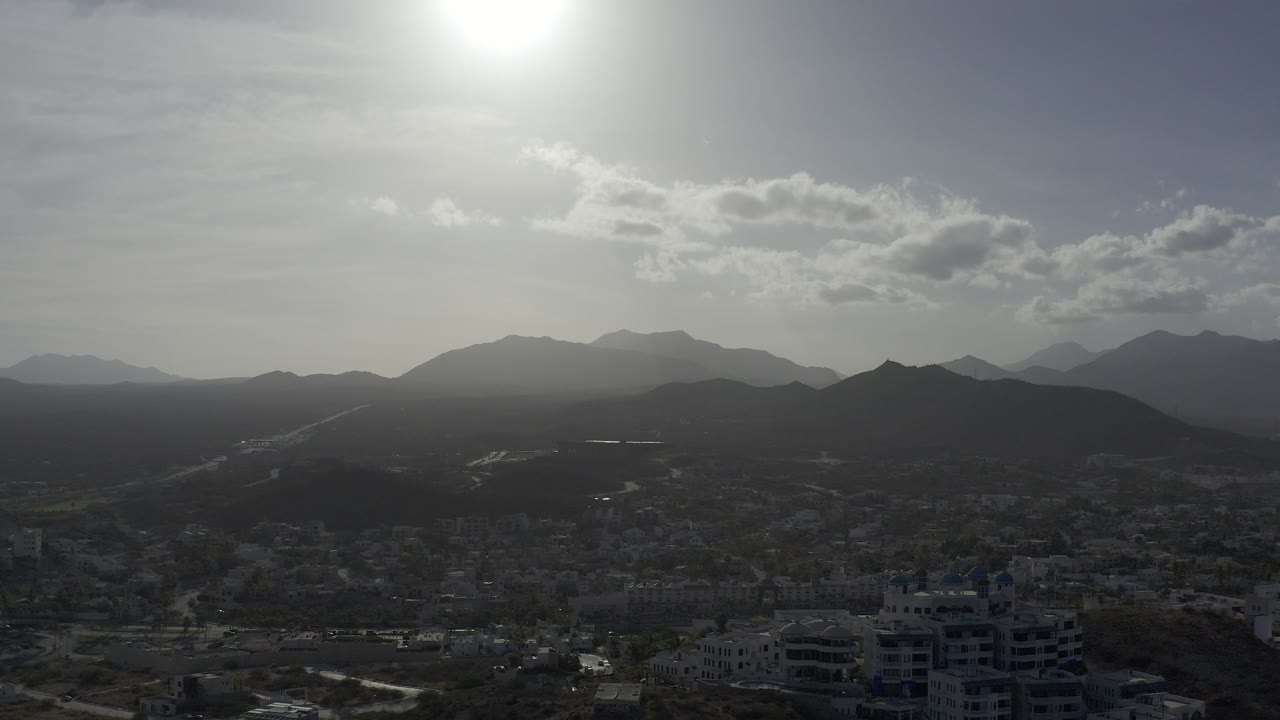 Hazy mountains and city under bright clouded sky.
