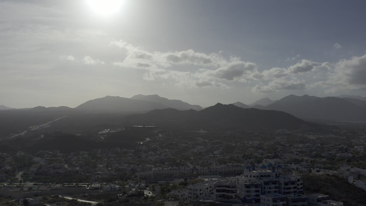 Bright sun over hazy mountains and a low town skyline.