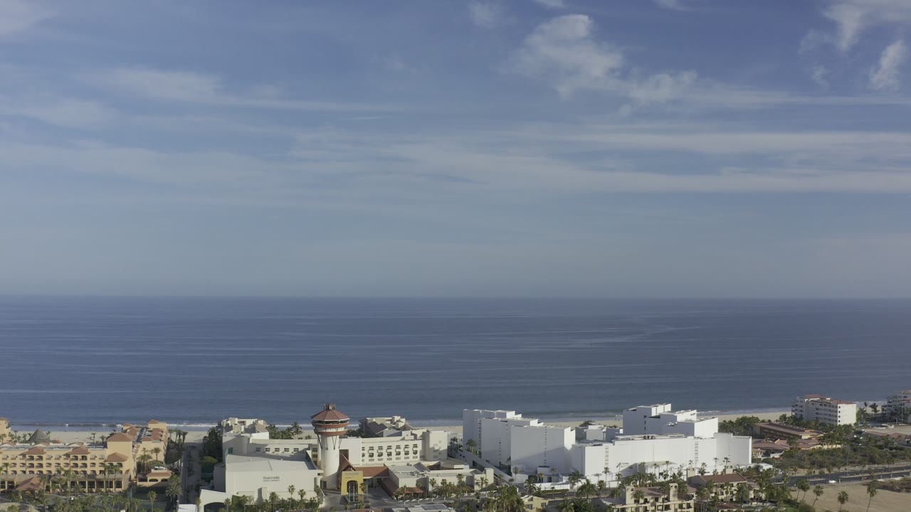 Aerial coastline scene with ocean, large white buildings, and trees.