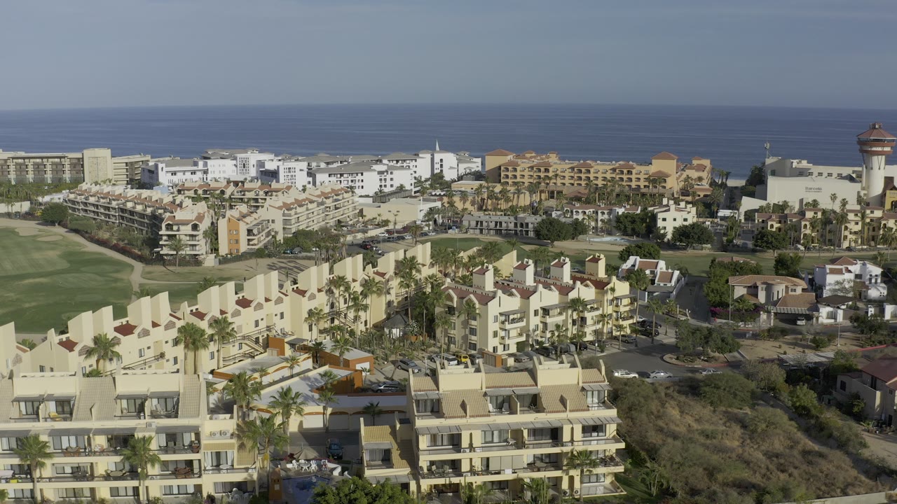 Aerial resort neighborhood with balconies, palms, lawns, and ocean beyond.