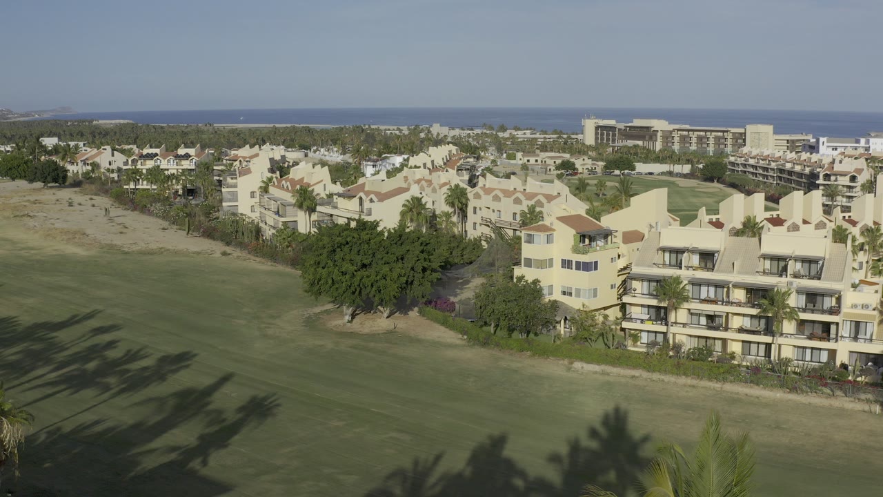 Elevated view of cream residential buildings beside a green field and ocean horizon.