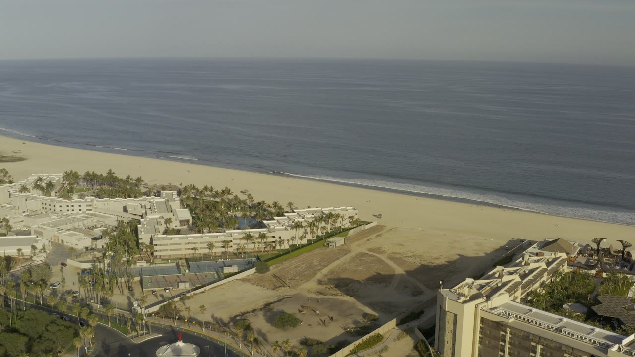 High aerial view of resort buildings, sandy beach, and ocean horizon.