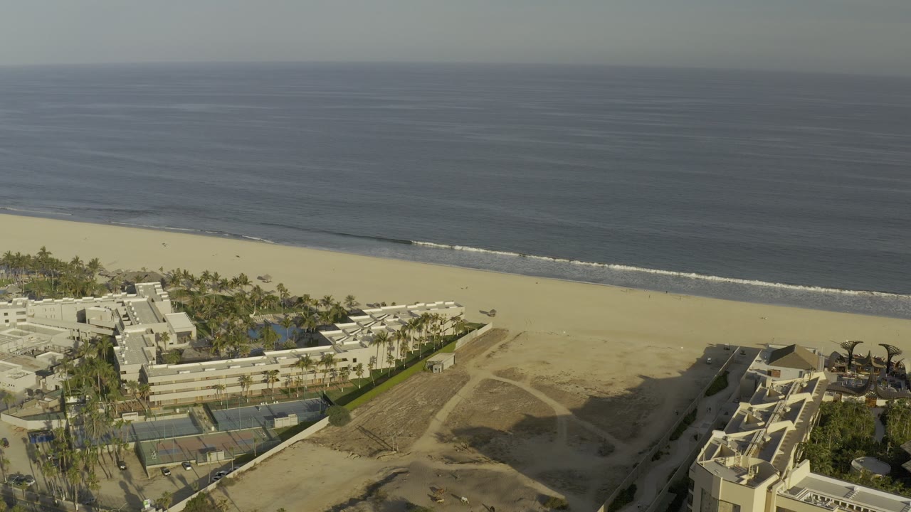 Aerial view of beach, ocean, palm trees, resort buildings, and tennis courts.
