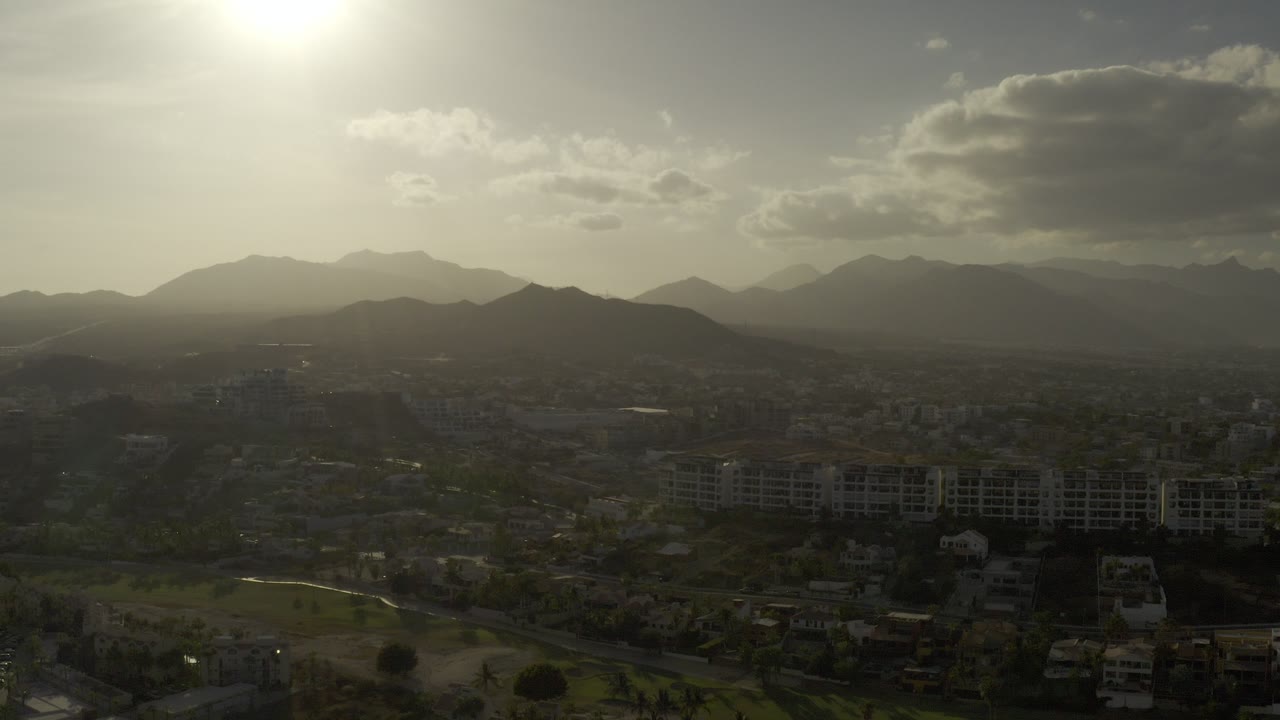 Hazy aerial view of mountains, buildings, and low sun.