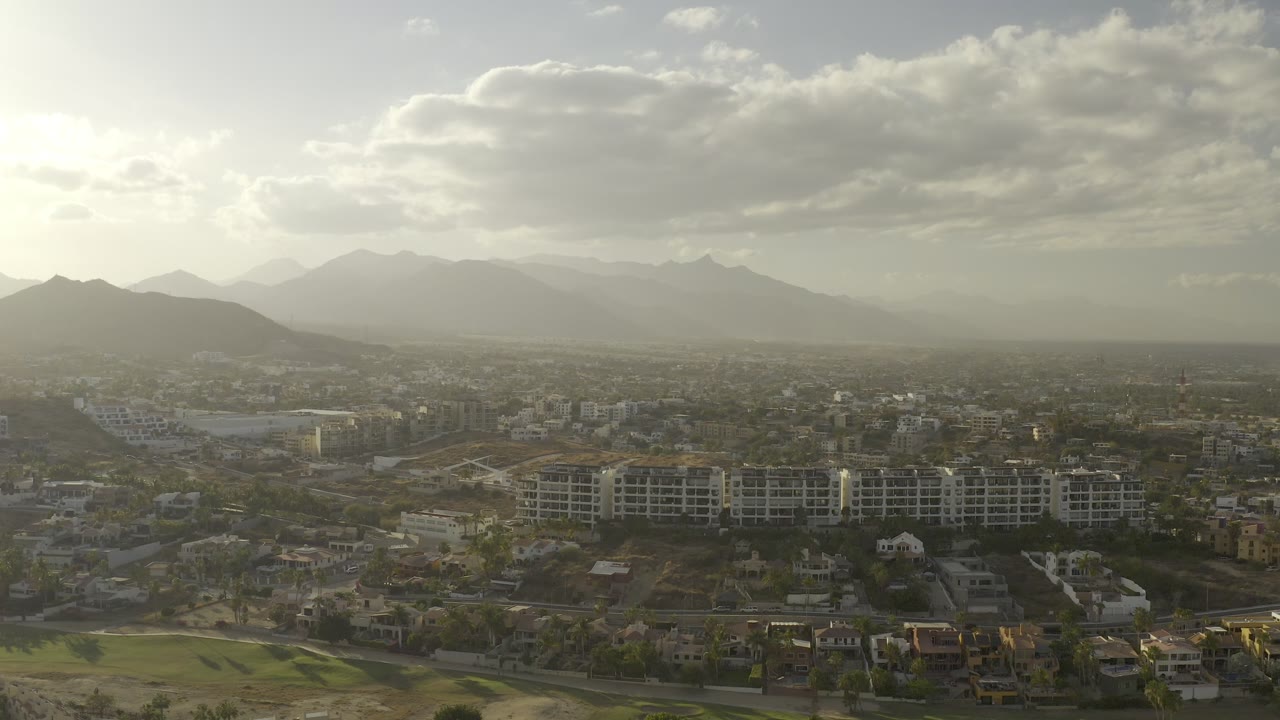 Aerial view of buildings, green course areas, mountains, and bright clouds.