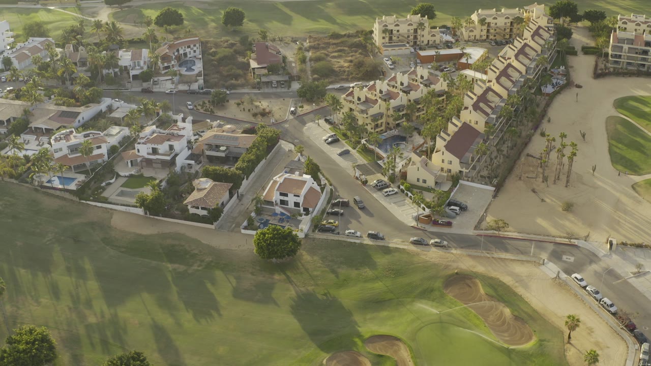 Aerial view of homes, roads, parked cars, and golf grass.