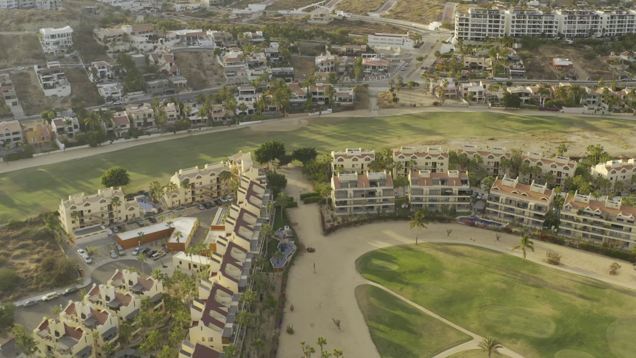 High aerial view of homes, a broad green area, and hillside development.