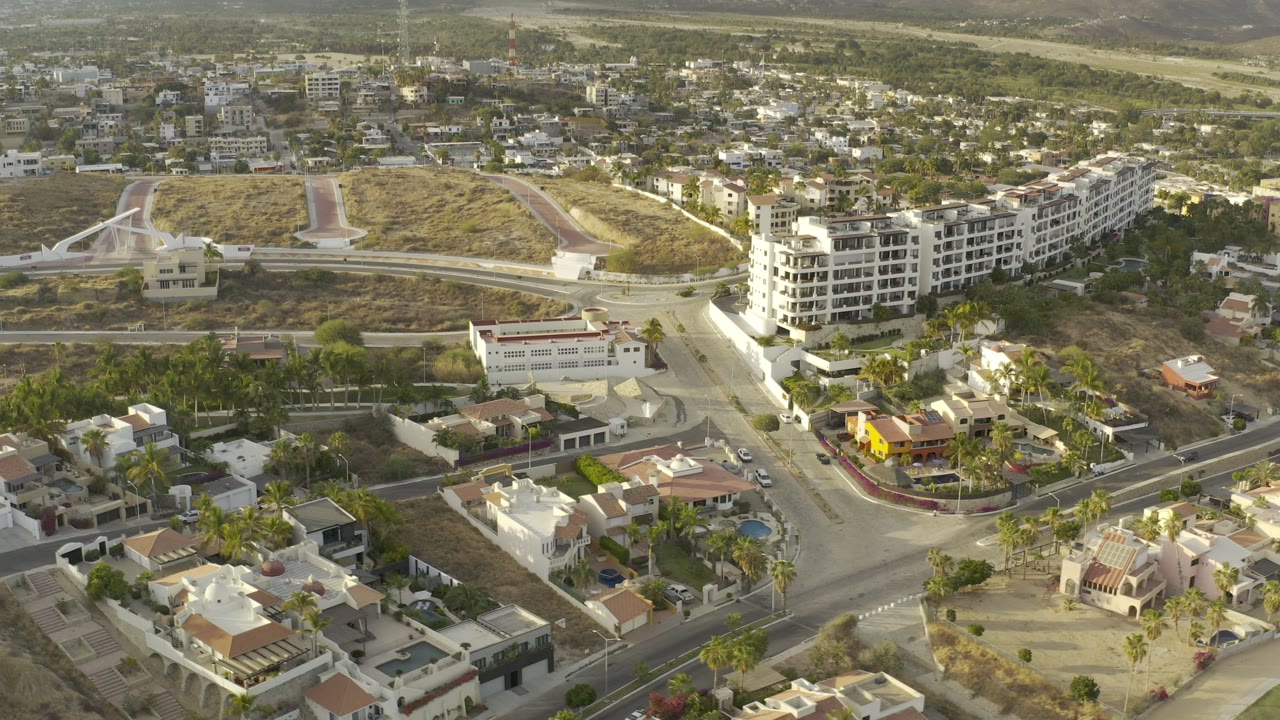 Aerial neighborhood view with a road junction, homes, and dry hillside paths.