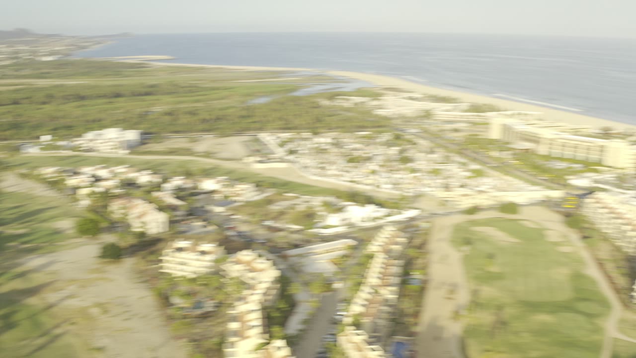 Wide aerial view of beachside buildings, golf grass, and ocean