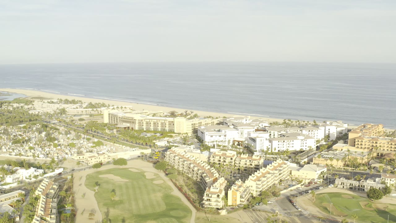 Aerial view of coastal buildings, golf course, beach, and ocean.