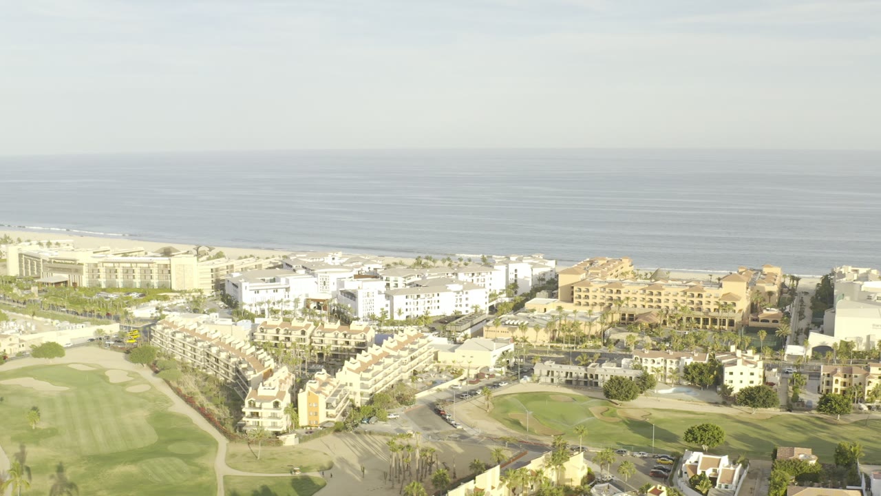 Aerial view of coastal homes, golf greens, and the sea horizon.
