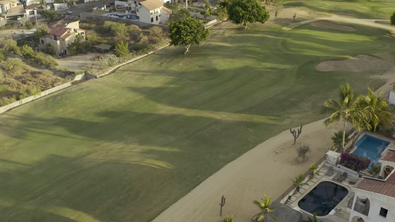Aerial view of a golf fairway beside villas and swimming pools.