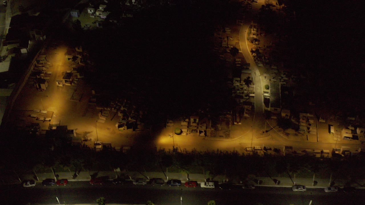 Night aerial view of streets, parked cars, and warm streetlights.