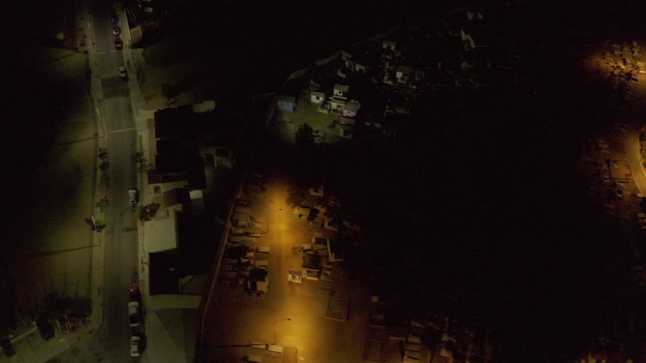Overhead night view of a lit residential street and rooftops.