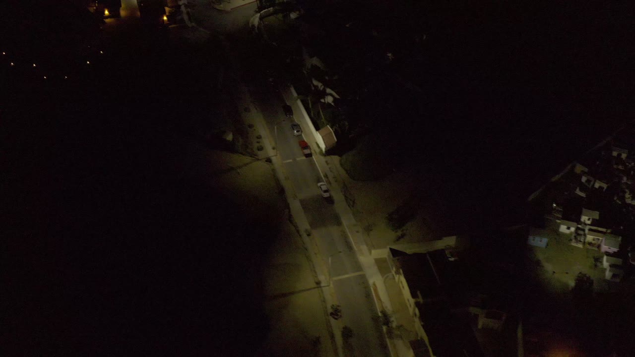 Dark aerial frame with a lit road and small residential buildings