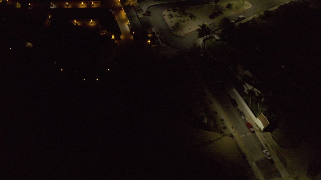 Opening overhead frame of Los Cabos at night, with warm streetlights outlining roads and buildings and no visible people.