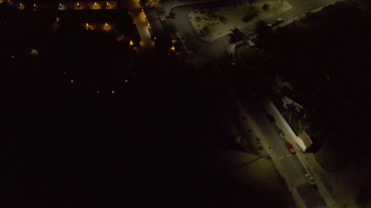 Second frame over Los Cabos at night, showing a lit street corner, building outlines, parked vehicles, and no visible people.